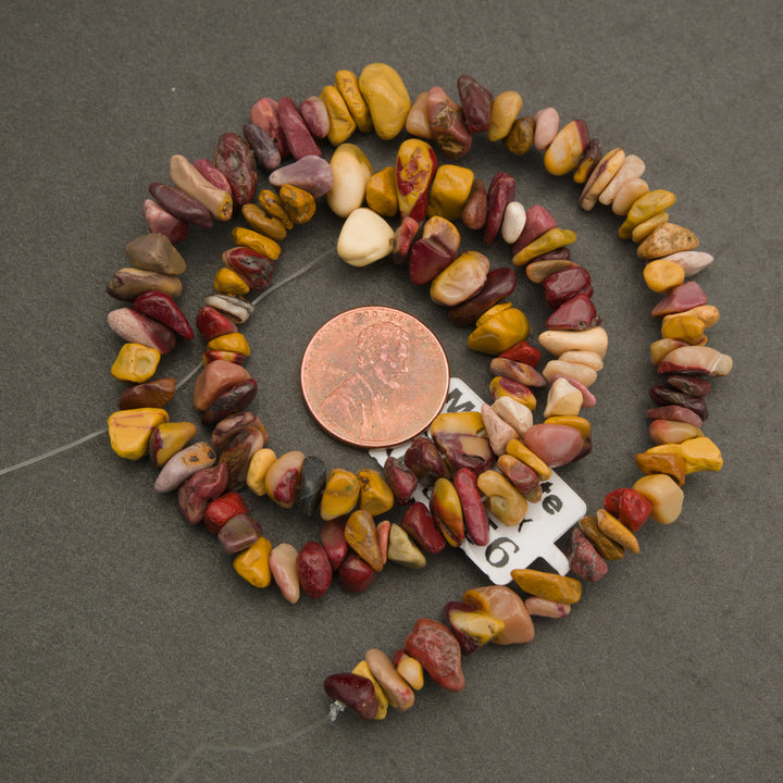Necklace made of multicolored stones with a penny for scale on a gray background