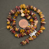 Necklace made of multicolored stones with a penny for scale on a gray background