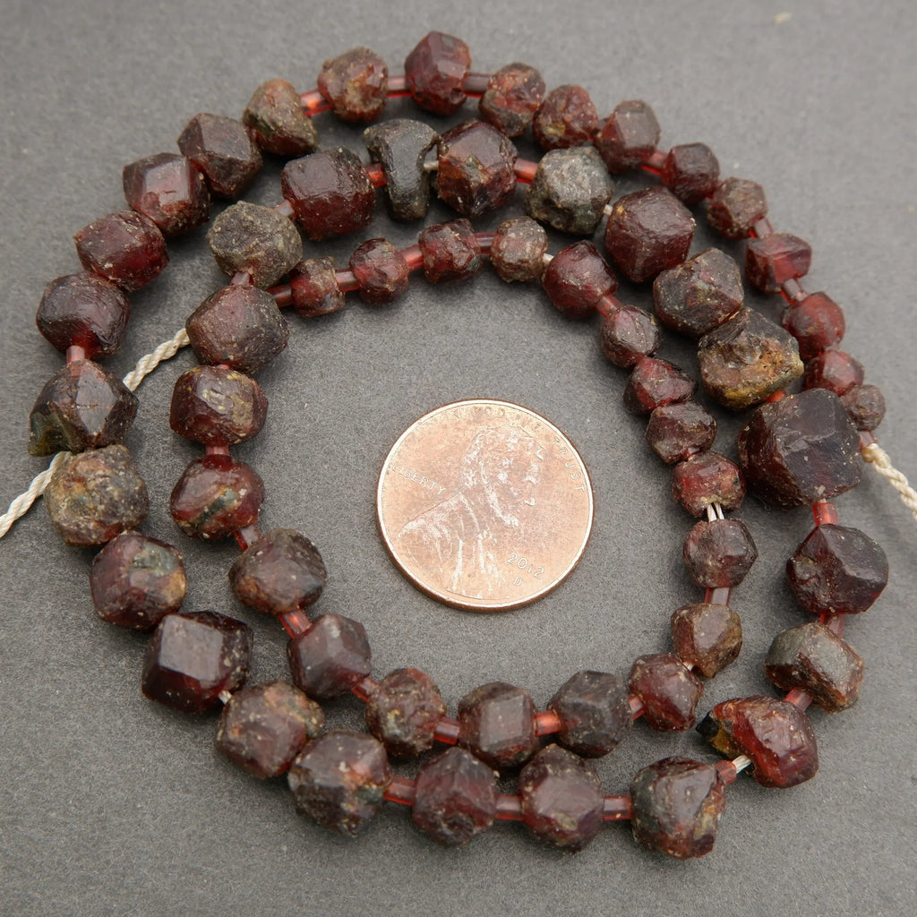 String of dark red beads with a penny for scale on a gray background