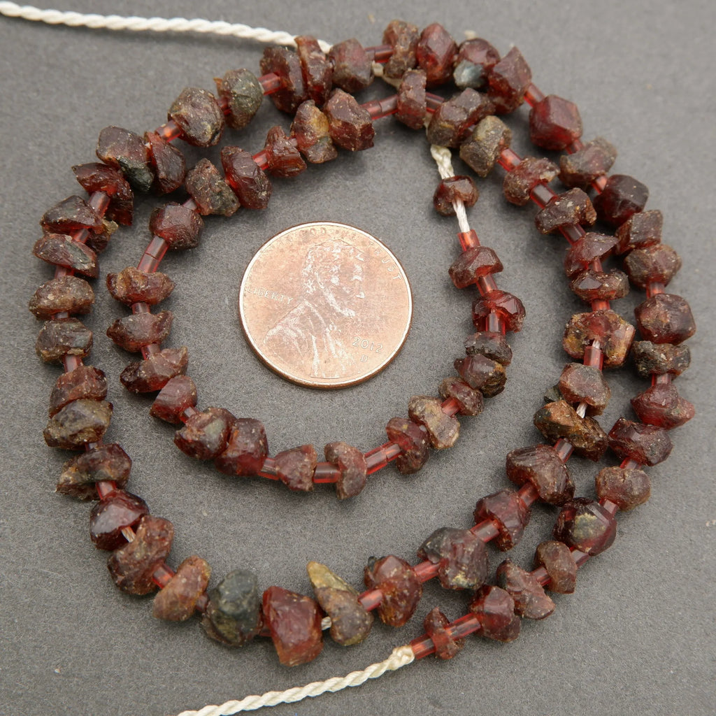 Necklace of red garnet beads with a penny for scale on a gray background