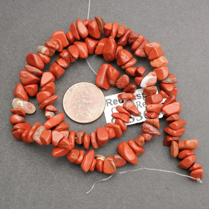 Red stone beads arranged in a circular pattern with a coin for scale on a gray background.