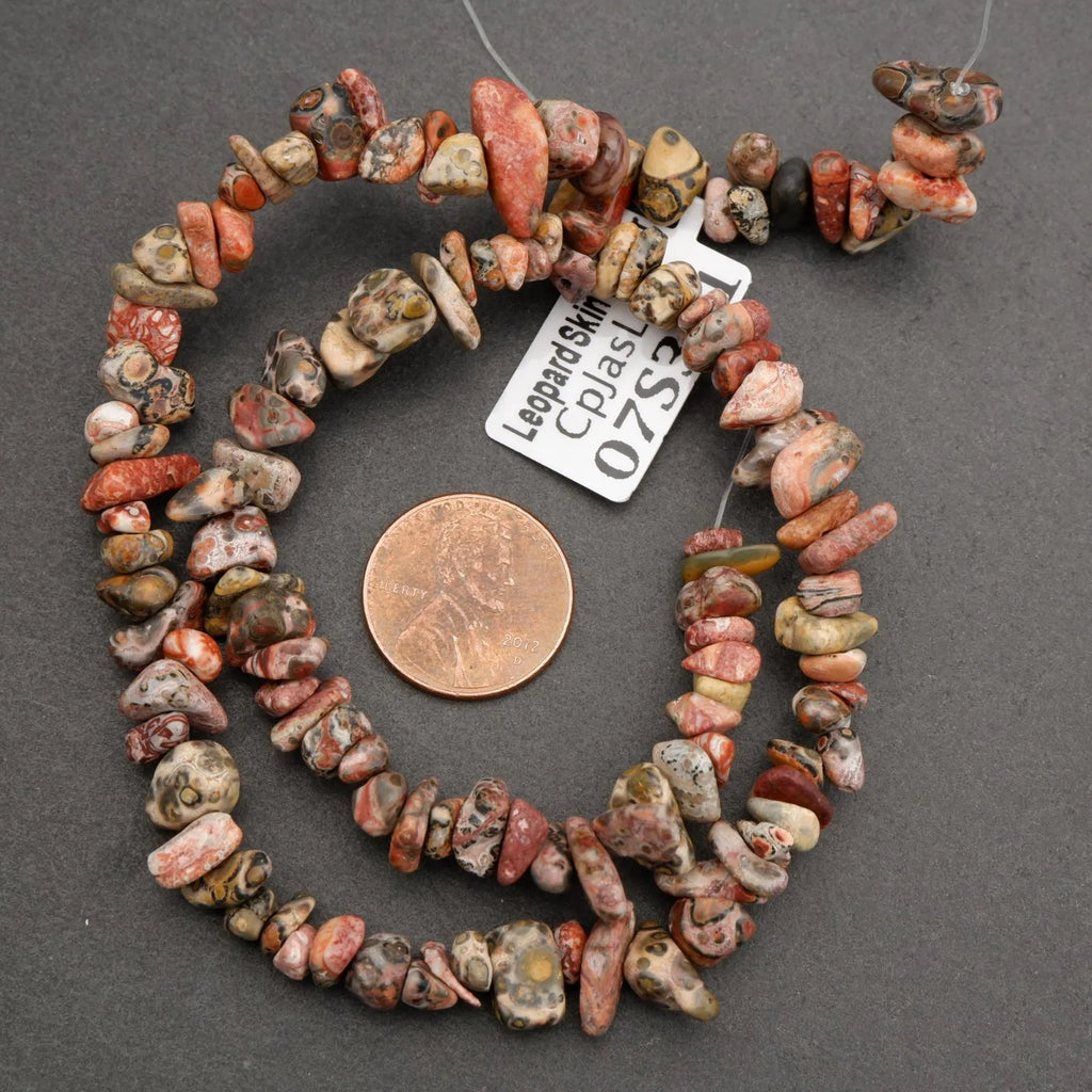 Necklace of multicolored beads with a penny for scale on a gray background