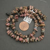 Necklace of multicolored stones with a penny for scale on a gray background