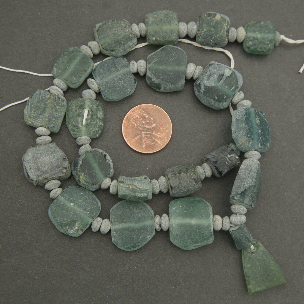 String of green beads with a penny for scale on a dark surface