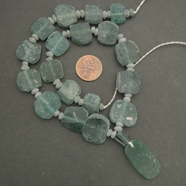 Necklace with green beads and a penny for scale on a gray background