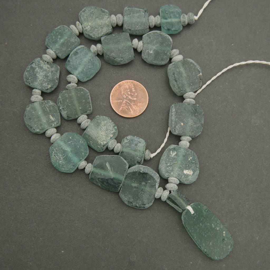 Necklace with green beads and a penny for scale on a gray background