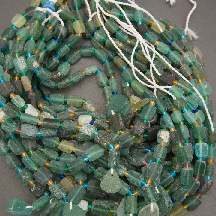 A pile of handmade beaded strands made of textured, translucent green glass beads with small blue and gold spacer beads, strung on white cords.