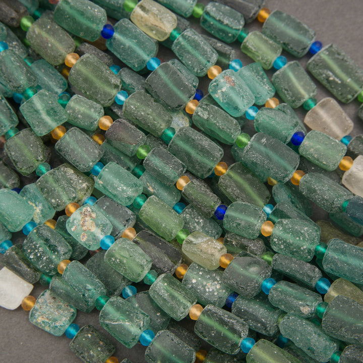 A pile of handmade beaded strands made of textured, translucent green glass beads with small blue and gold spacer beads, strung on white cords.