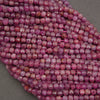 Faceted pink gemstone beads arranged in a curved stack on a neutral gray background.