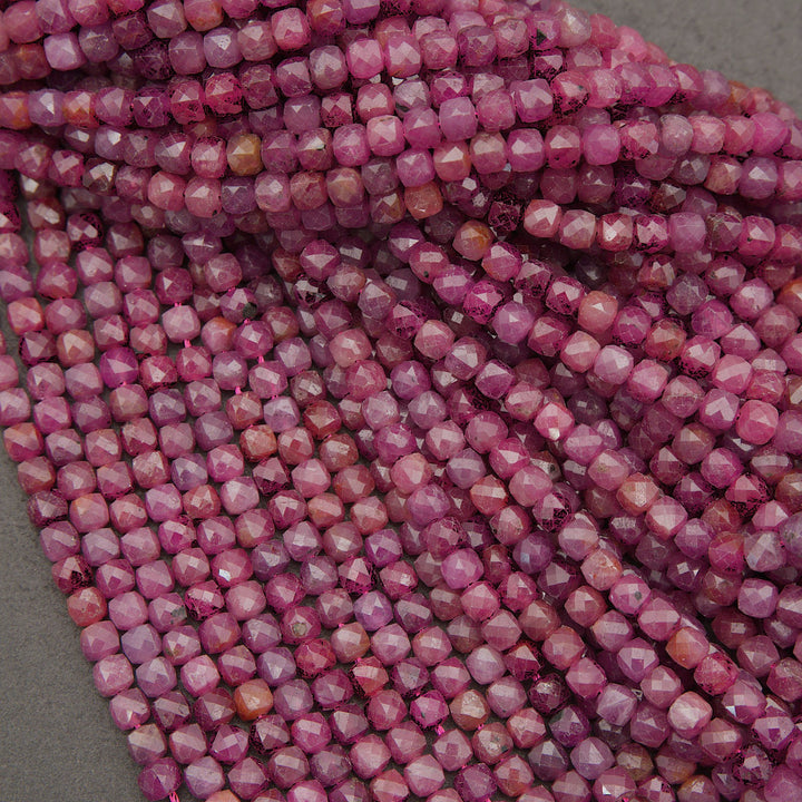 Close-up of multiple strands of faceted round beads in a pink to magenta gradient, arranged diagonally on a gray surface.