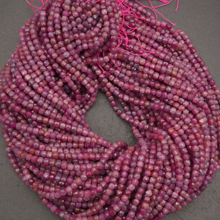 A coiled bundle of faceted gemstone beads in a marbled mix of pink, purple, and red tones, strung on bright pink thread against a neutral gray background.