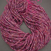 A coiled bundle of faceted gemstone beads in a marbled mix of pink, purple, and red tones, strung on bright pink thread against a neutral gray background.