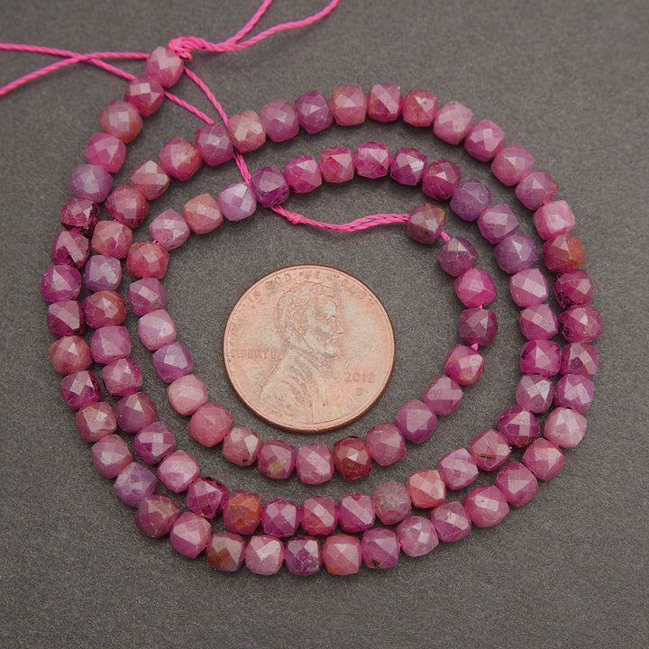 Faceted pink gemstone beads on a pink string, shown in a coiled arrangement with a US penny for scale on a dark gray background.
