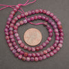 Faceted pink gemstone beads on a pink string, shown in a coiled arrangement with a US penny for scale on a dark gray background.