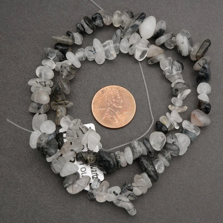 Necklace with small stones and a penny for scale on a gray background