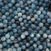 A close-up pile of round blue gemstone beads with natural marbling and variations in light and dark blue tones.