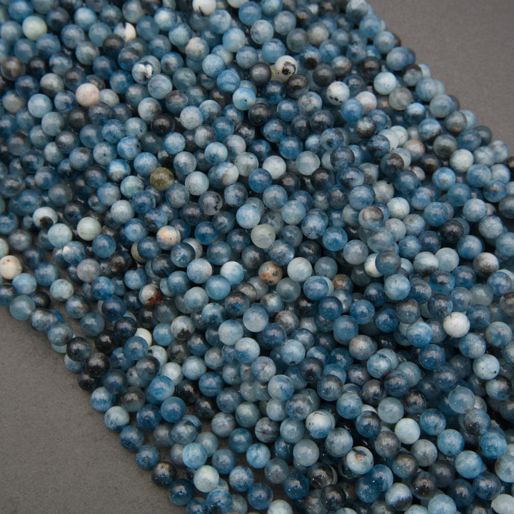 A close-up of multiple strands of round blue stone beads, likely lapis lazuli, arranged diagonally on a dark gray background.