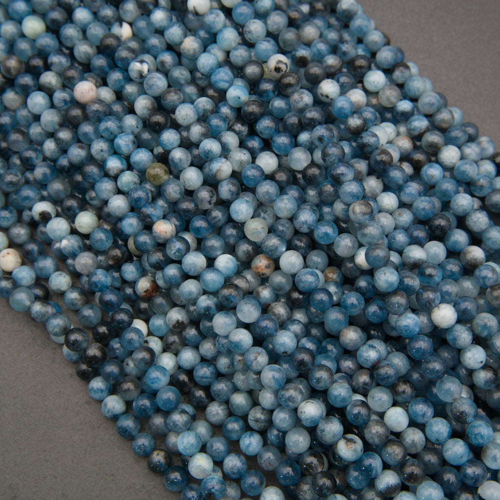 A close-up of multiple strands of round blue stone beads, likely lapis lazuli, arranged diagonally on a dark gray background.