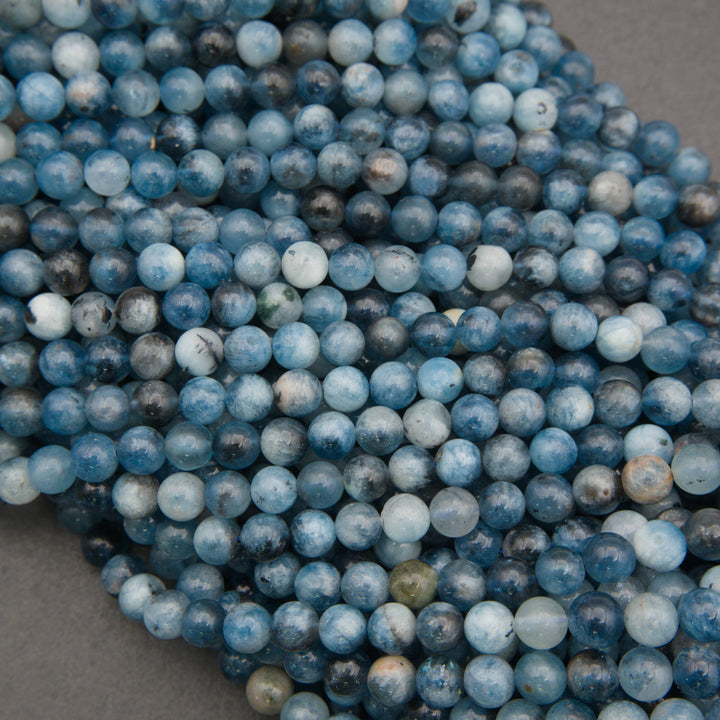 A close-up pile of round blue marbled beads with white and gray veining, resting on a neutral gray surface.