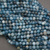 A close-up pile of round blue marbled beads with white and gray veining, resting on a neutral gray surface.