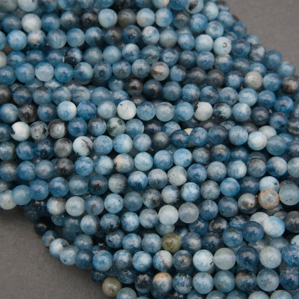 A close-up pile of round blue marbled beads with white and gray veining, resting on a neutral gray surface.