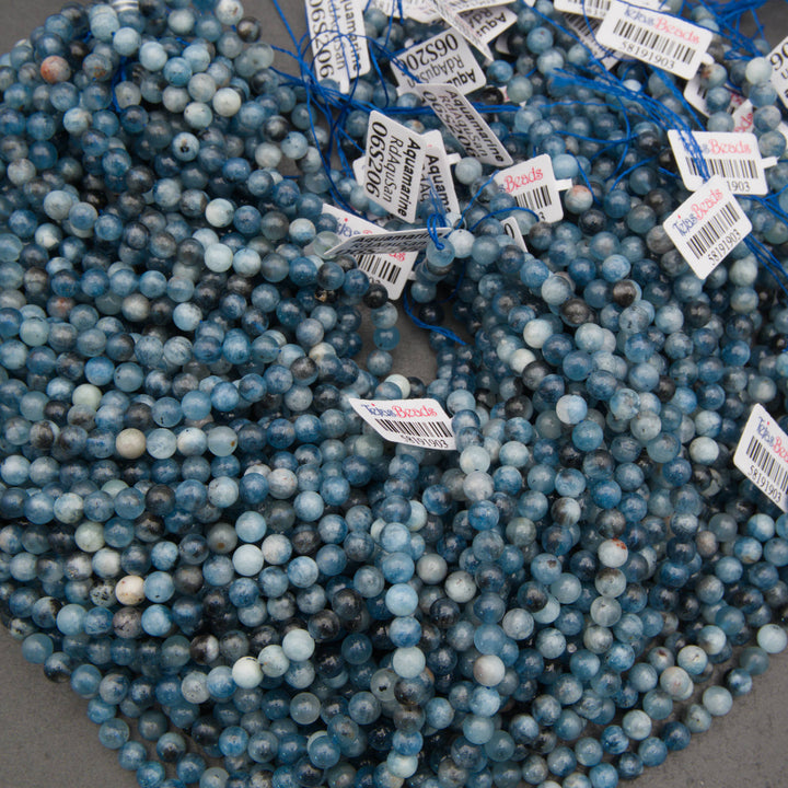 A pile of round blue gemstone beads with white price tags attached, photographed close-up on a neutral surface.