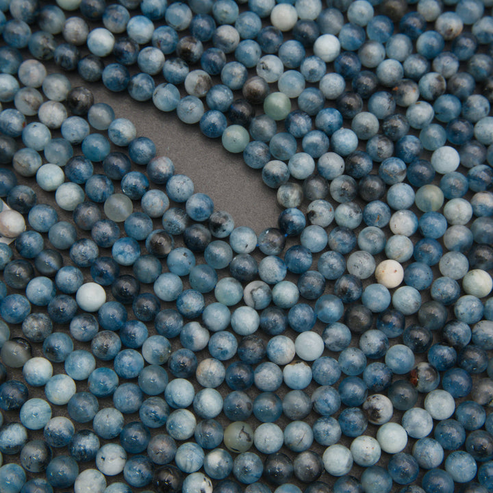 A close-up of many small round blue marbled beads scattered across a gray surface, with no person, animal, or real environment visible.