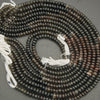 String of black and brown beads with white tassels on a gray background