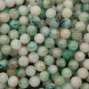 Close-up of smooth round Sky Mountain Jade beads in creamy white and pale mint with teal green flecks and a few deep blue spots
