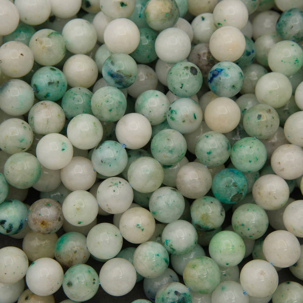 Close-up of smooth round Sky Mountain Jade beads in creamy white and pale mint with teal green flecks and a few deep blue spots