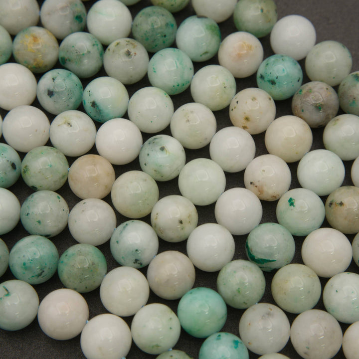 Rows of smooth round Sky Mountain Jade beads on a gray background, creamy white with teal green speckles