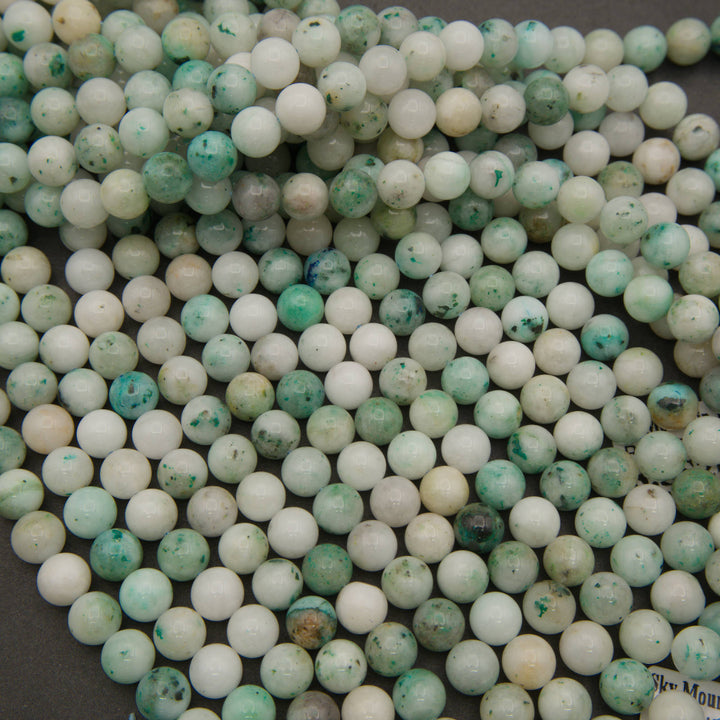 Rows of smooth round Sky Mountain Jade bead strands on a gray background
