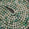 Strands of smooth round Sky Mountain Jade beads laid in curving rows on a dark gray background, in white, mint and teal
