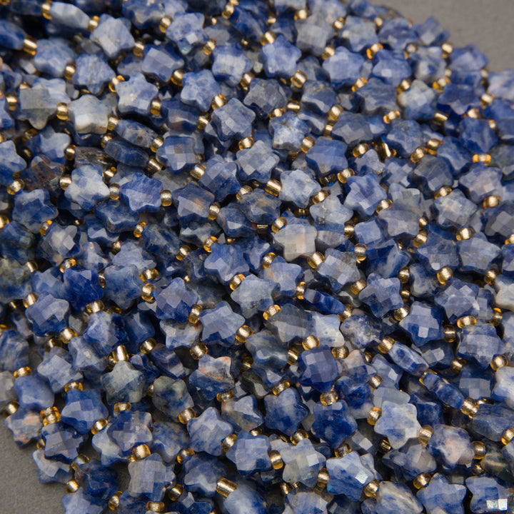A heap of faceted snowflake sodalite star bead strands in royal blue with white patches and gold seed bead spacers
