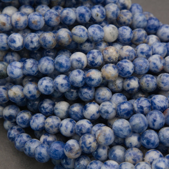 Multiple strands of small round beads in a marbled blue and white pattern, with several white product tags attached, photographed on a gray surface.
