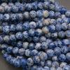 Multiple strands of small round beads in a marbled blue and white pattern, with several white product tags attached, photographed on a gray surface.
