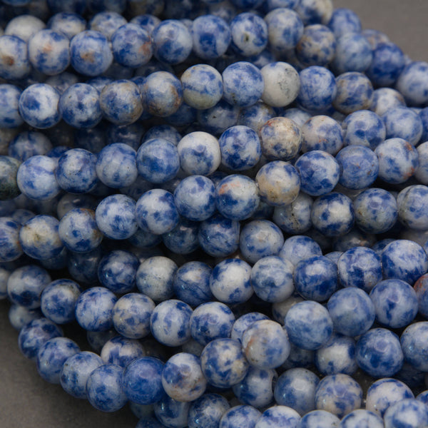 Multiple strands of small round beads in a marbled blue and white pattern, with several white product tags attached, photographed on a gray surface.