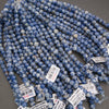 Multiple strands of small round beads in a marbled blue and white pattern, with several white product tags attached, photographed on a gray surface.