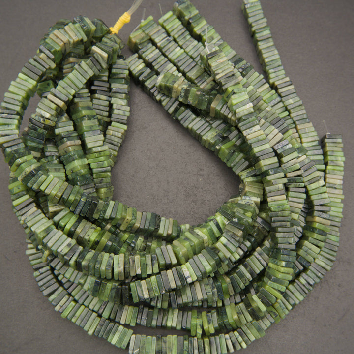 Green stone bead strands made of small rectangular disc-like beads, arranged on a dark gray background.