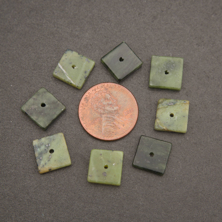 Eight small square green stone beads with a central hole, arranged in a circle around a copper penny on a dark gray background.