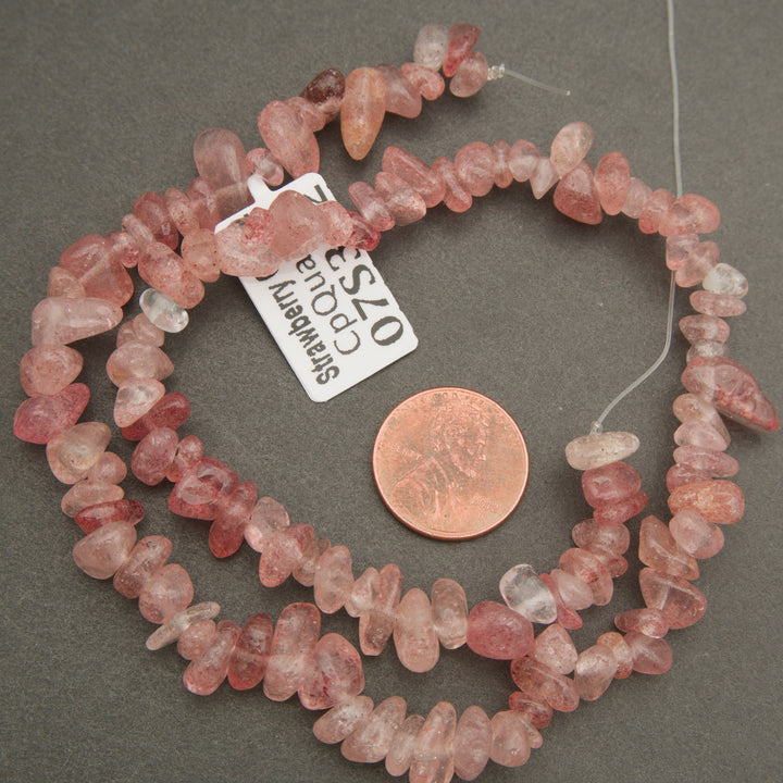 Necklace of pink stone beads with a penny for scale on a gray.background