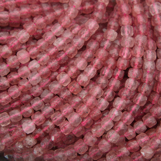 Close-up of strands of faceted pinkish-red beads, likely rose quartz, showing a translucent pink color with natural inclusions.