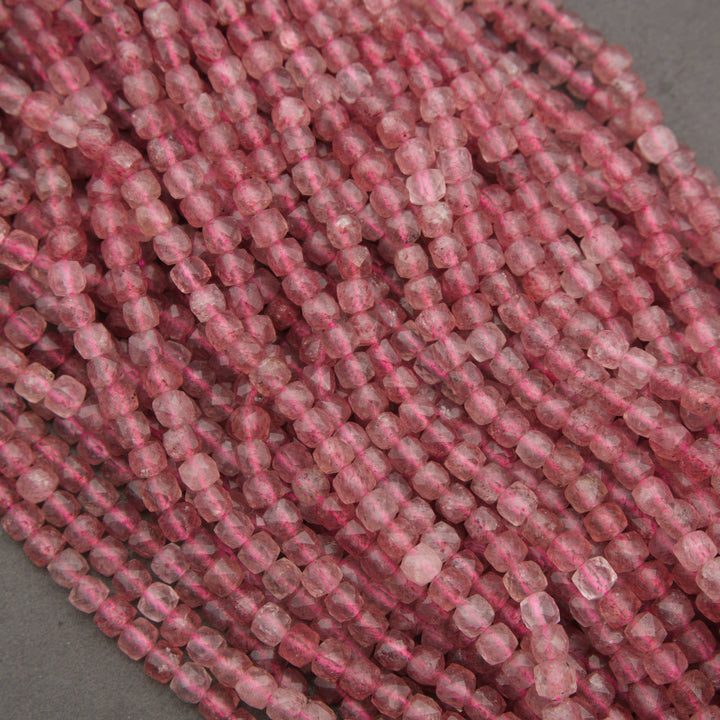 A close-up of multiple strands of faceted pink beads, likely rose quartz, arranged on a neutral gray background.