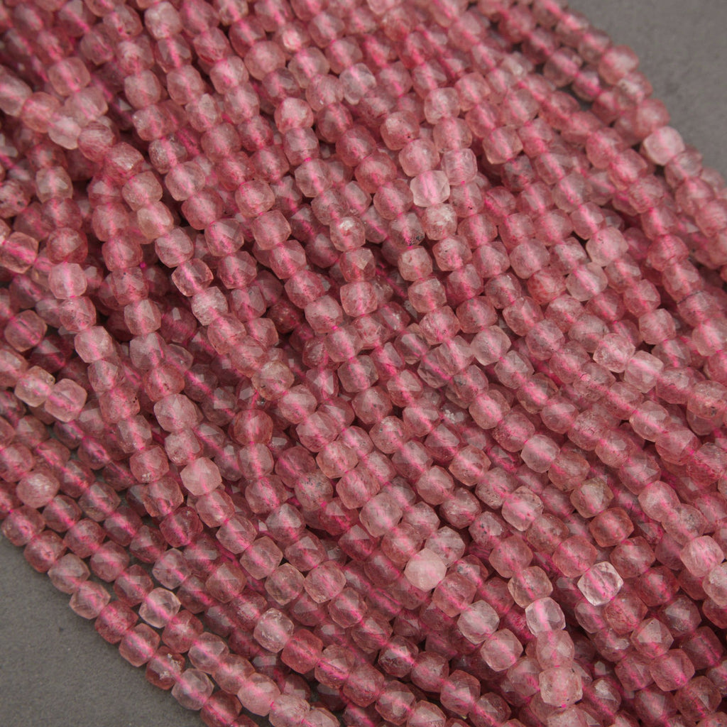 A close-up of multiple strands of faceted pink beads, likely rose quartz, arranged on a neutral gray background.