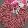 A close-up of a coiled bundle of small, faceted pink beads on a neutral gray background.