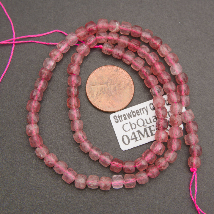 A close-up of a coiled bundle of small, faceted pink beads on a neutral gray background.