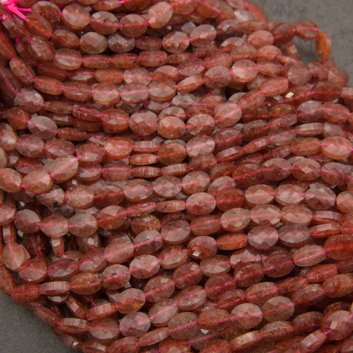 Strands of faceted strawberry quartz oval beads in rows on a gray background, with glittering red flecks