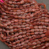 Strands of faceted strawberry quartz oval beads in rows on a gray background, with glittering red flecks