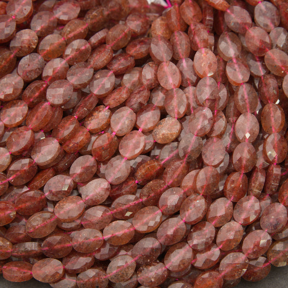 Close-up of faceted strawberry quartz oval beads showing translucent pink stone with tiny red flecks