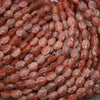Close-up of faceted strawberry quartz oval beads showing translucent pink stone with tiny red flecks